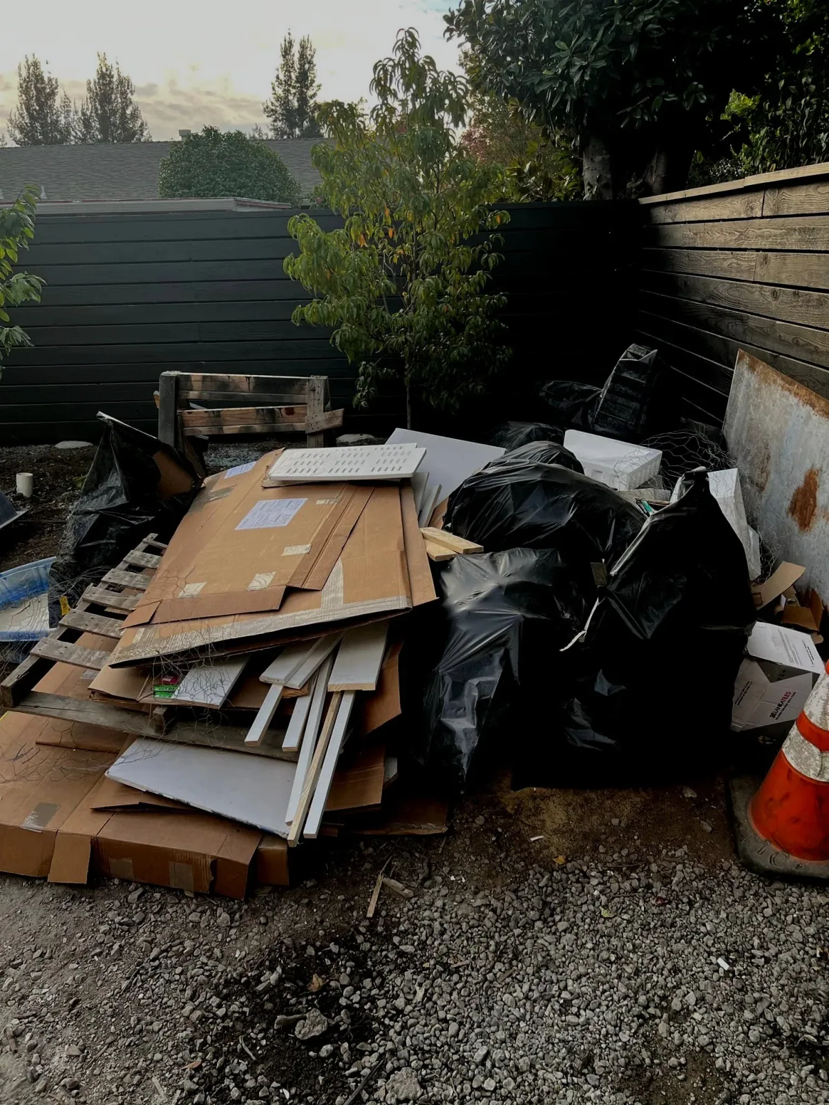 Bagged waste and loose materials beside a wooden fence